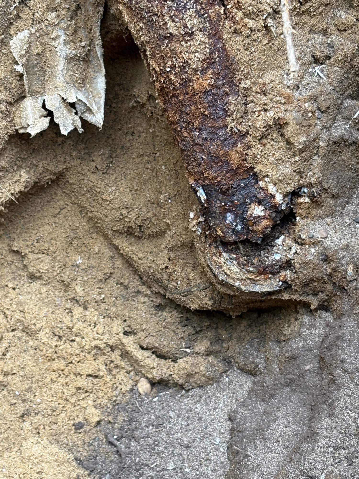 Corroded underground service pipe uncovered in sandy soil